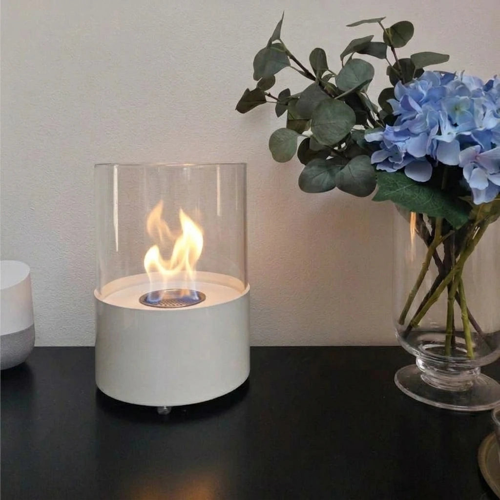 Kennington round white tabletop bioethanol fireplace lit on a table with blue flowers