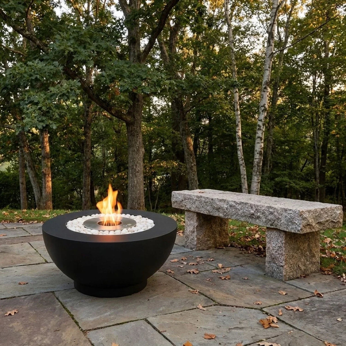 ScandiFlames Circula black bioethanol fire pit burning on a stone patio beside a woodland garden